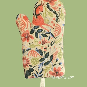 Könnte beinhalten: Ein Ofenhandschuh mit rotem und grünem Blumendruck und einem stilisierten Hirschdesign. Der Handschuh hat eine Aufhängeschlaufe und der Text "ithinksew.com" ist unten aufgedruckt.