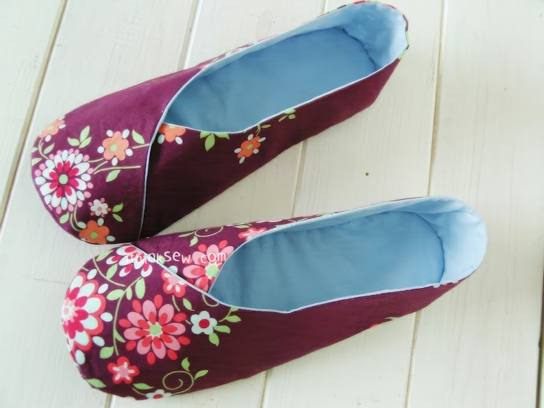 May include: A pair of burgundy fabric slippers with a floral pattern in pink, orange, and green. The interior is a light blue fabric. The slippers are designed for indoor use and comfort.