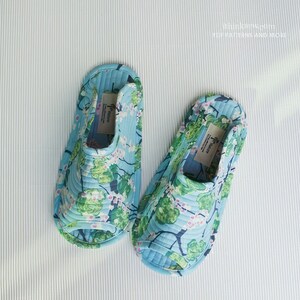 Op de afbeelding: Een paar blauwe en groene slippers met bloemenprint. De slippers hebben een gestikt ontwerp en zijn open.
