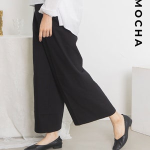 May include: A woman is wearing black wide-leg pants and black flats. The pants have a wide leg and a relaxed fit. The flats are simple and stylish. The word "MOCHA" is written in white letters on a black background in the upper right corner of the image.