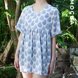 May include: A white dress with a blue leaf pattern. The dress has a v-neck and short sleeves. The dress is loose fitting and has a gathered waist.