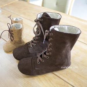 May include: Two pairs of brown suede lace-up boots. The larger pair has a brown suede upper and a white lining. The smaller pair is a lighter brown suede with a brown lining. Both pairs have brown laces and metal eyelets.