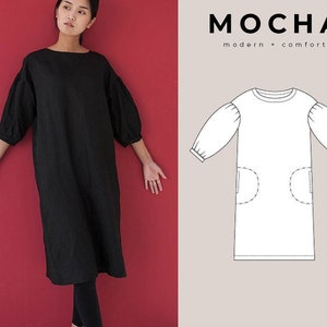 May include: A black, long-sleeved dress with a round neckline and puffed sleeves. The dress has two pockets on the front and falls to the knees. The dress is shown on a model against a red background.