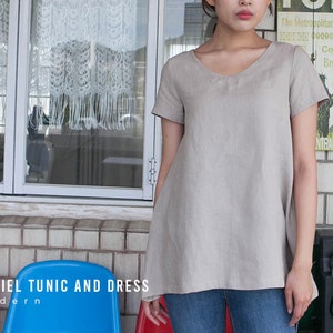 May include: A light gray linen tunic with a v-neck and short sleeves. The tunic is loose fitting and falls to the hips. The model is wearing the tunic with blue jeans.