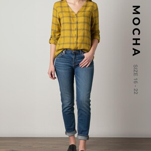 以下が含まれることがあります： マスタードイエローのチェック柄シャツとブルージーンズを着た女性。シャツはVネックと長袖です。ジーンズは足首で折り返されています。「MOCHA」の文字とサイズ「16-22」が右側に印刷されています。