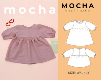 May include: A sewing pattern for a long-sleeved dress with a gathered skirt. The pattern is available in sizes 3Y to 10Y. The dress is shown in a light pink color. The pattern is called "MOCHA modern + comfort".