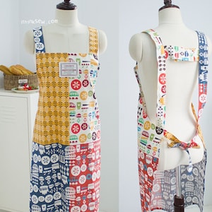 May include: A colourful patchwork apron with a white background and a variety of patterns, including flowers, geometric shapes, and a small label that says "Cinnamon". The apron has adjustable straps and a tie at the back.