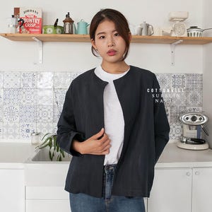 Może przedstawiać: Granatowa kurtka z lnu i bawełny z okrągłym dekoltem i długimi rękawami. Kurtka jest rozpięta, a osoba, która ją nosi, stoi w kuchni.