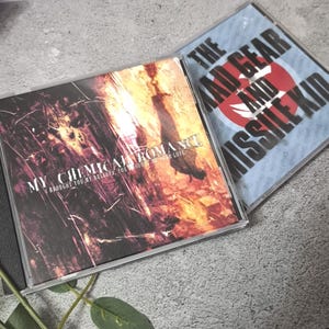Puede incluir: Dos CD en estuches transparentes. Uno presenta el texto "MY CHEMICAL ROMANCE" y "I BROUGHT YOU MY BULLETS, YOU BROUGHT ME YOUR LOVE". El otro estuche de CD tiene el texto "THE MAD GEAR AND MISSILE KID".