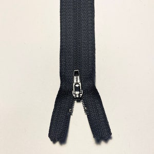 May include: A black zipper with a silver slider. The zipper is open and the slider is in the middle.