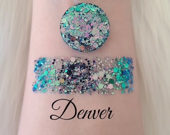 May include: A swatch of iridescent glitter in shades of teal, blue, and pink, with the word "Denver" in cursive script. A circular sample of the same glitter is above the swatch. The glitter is likely for cosmetic use.