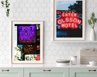May include: Two framed wall art prints featuring neon signs. The left print displays the purple text FAT TUES DAY. The right print shows a red neon sign with the text ENTER OLSSON MOTEL and a green arrow, set against a dark background.