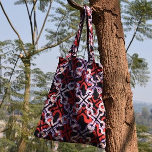 May include: A red, black and white patterned tote bag with two handles hanging from a tree branch.
