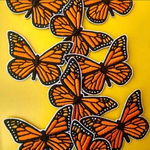 May include: A collection of orange and black butterfly iron-on patches. The patches are embroidered with intricate details and have a slightly textured surface.