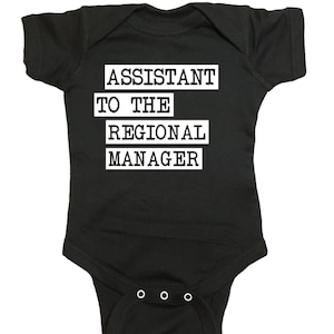 Può includere: Body per neonati nero con la scritta bianca "ASSISTANT TO THE REGIONAL MANAGER". Il body ha maniche corte e tre bottoni automatici sul fondo.
