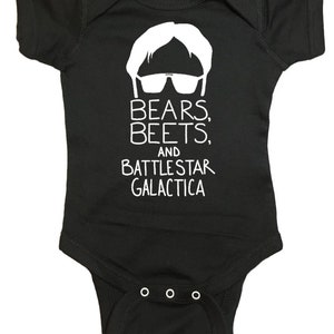 Puede incluir: Un body negro para bebé con un gráfico blanco de un hombre con gafas de sol y el texto "Bears, Beets, and Battlestar Galactica."