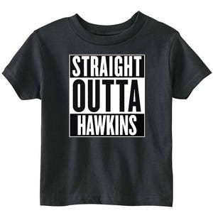 Puede incluir: Una camiseta gris oscuro con un gráfico blanco que dice "STRAIGHT OUTTA HAWKINS" en un cuadro negro.