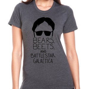 Puede incluir: Una camiseta gris oscuro jaspeada con una silueta negra de un hombre con gafas de sol y el texto "Bears, Beets, and Battlestar Galactica".
