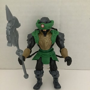 May include: A green and black action figure with a gray spear. The figure is wearing a green helmet with a red circle on the front. The figure is holding the spear in its right hand.