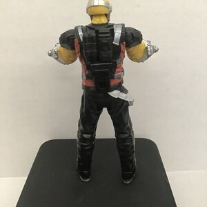 May include: A black and red action figure with a yellow helmet and silver accents. The figure is wearing a black and red suit with a black backpack. The figure is standing on a black surface.