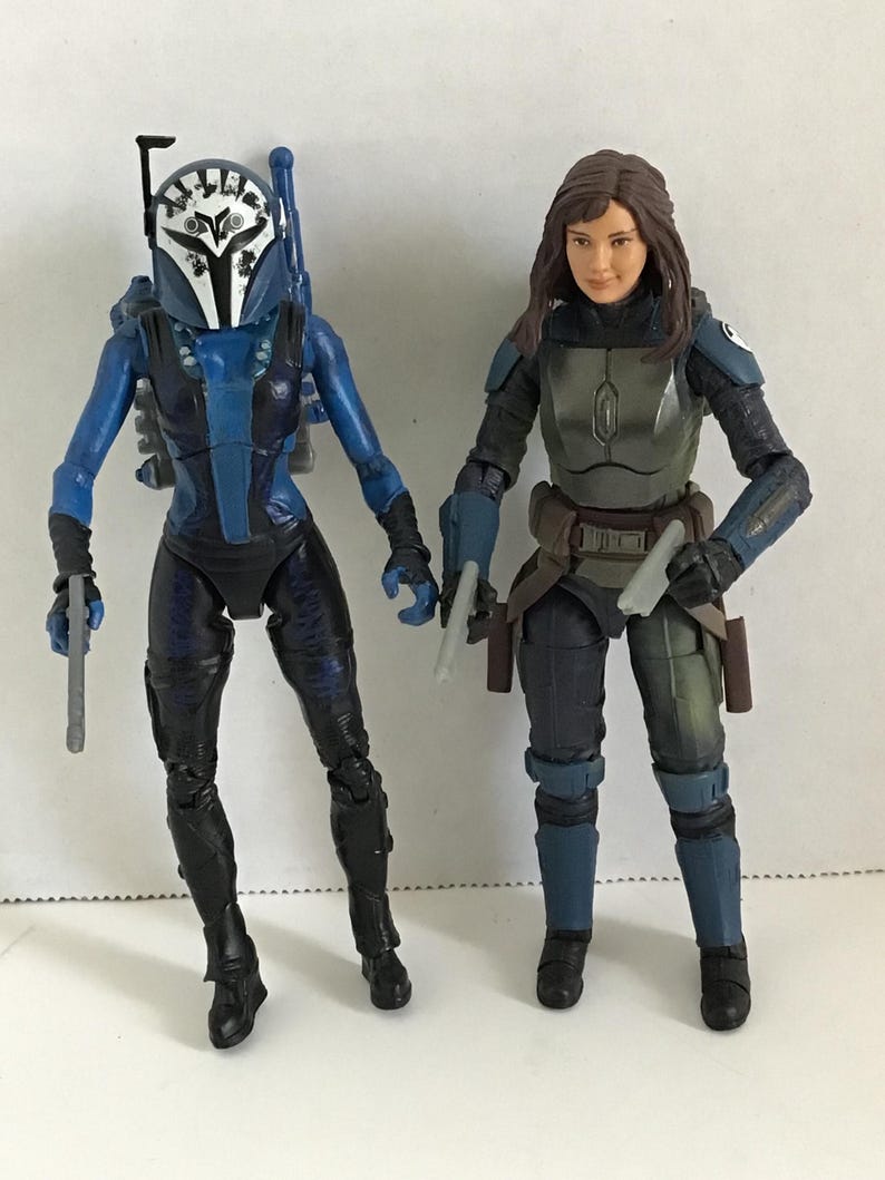 May include: Two action figures of characters in combat gear. One figure is in blue and black armor with a helmet. The other figure is in gray and black armor. Both figures are holding weapons and standing on a white surface.