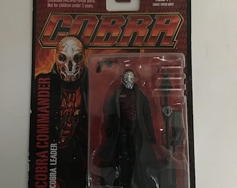 May include: A Cobra Commander action figure in its original packaging. The figure is in a clear plastic case, with a black and red card featuring the Cobra logo and the words "COBRA COMMANDER" and "COBRA LEADER". The packaging includes a warning about small parts.