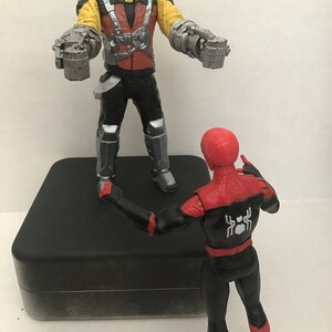 May include: A red and black Spider-Man action figure stands on a black platform facing a yellow and red action figure with silver robotic arms. The figure with robotic arms is wearing a black helmet with a silver visor.