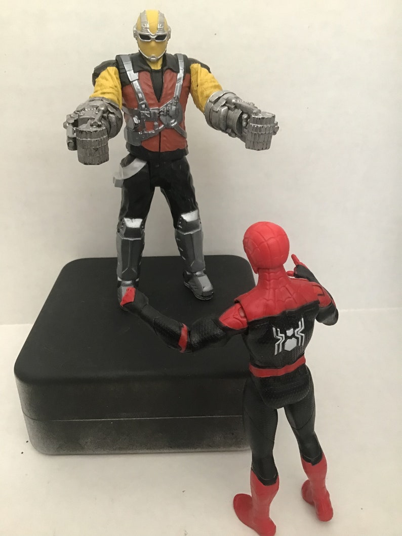 May include: A red and black Spider-Man action figure stands on a black platform facing a yellow and red action figure with silver robotic arms. The figure with robotic arms is wearing a black helmet with a silver visor.