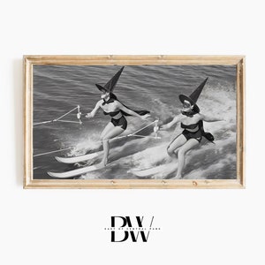 May include: Two women dressed as witches water ski on a lake. They are wearing black swimsuits and witch hats. The photo is in black and white.