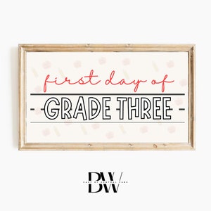 May include: A framed sign with the words "first day of GRADE THREE" in red and black. The background is cream-colored with pencil and apple illustrations. The sign is a decorative item for a classroom or home, with a wooden frame.