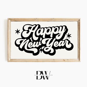May include: A framed print with the words "Happy New Year" in bold, black, retro-style lettering. The text is centered on a cream-colored background, with star accents. The frame is a light wood color.