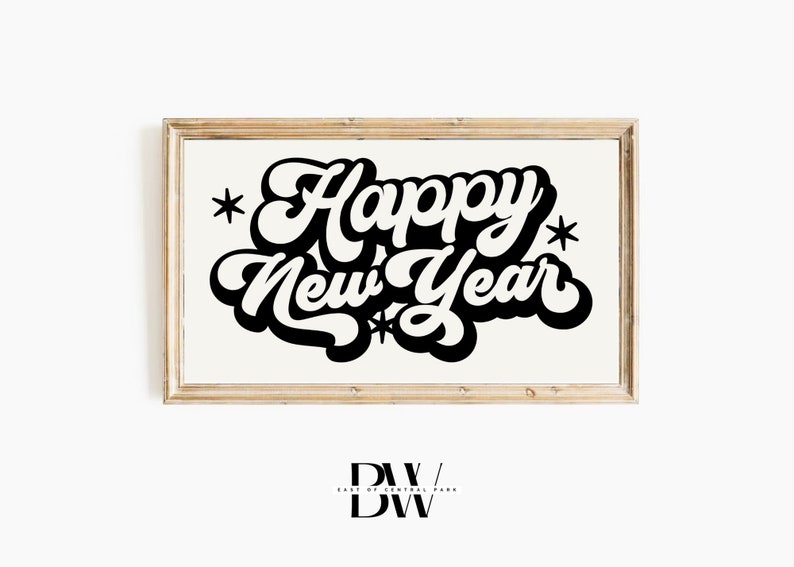May include: A framed print with the words "Happy New Year" in bold, black, retro-style lettering. The text is centered on a cream-colored background, with star accents. The frame is a light wood color.