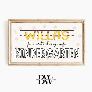 May include: A wooden framed sign with the text "Willa's first day of Kindergarten." The name "Willa's" is written in yellow pencil-shaped letters. The sign has a light background with apple and pencil illustrations.