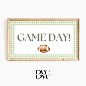 May include: A framed printable sign with a green and white gingham border. The sign says "GAME DAY!" with a brown football illustration in the centre.