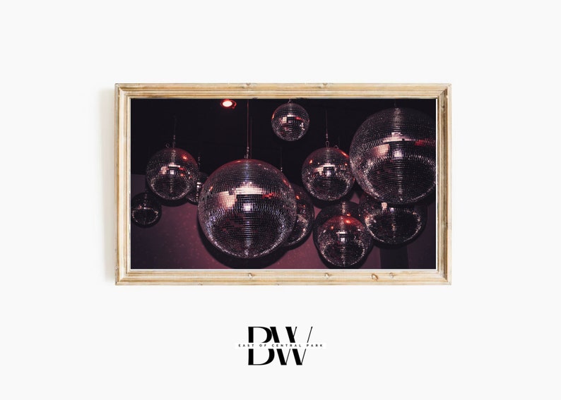 May include: A framed print featuring multiple disco balls hanging from a dark ceiling. The mirrored spheres reflect light, creating a sparkling effect. The frame is a light wood color. The image has a vintage, retro aesthetic.