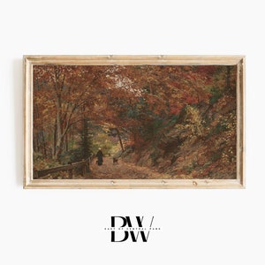 May include: Framed vintage landscape art print. The artwork shows a person walking a dog on a path through a forest in autumn. The trees have red, orange, and yellow leaves. The frame is a light wood colour.