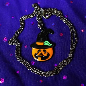 May include: A black chain necklace with a pumpkin-shaped pendant. The pumpkin is orange with a black face and a green hat.
