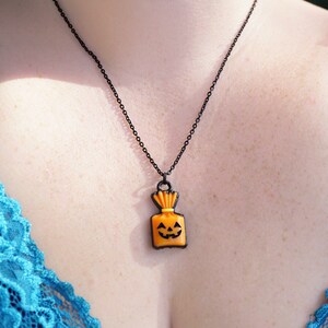 May include: A black chain necklace with an orange pumpkin-shaped pendant. The pendant has a black outline and a smiling jack-o'-lantern face.