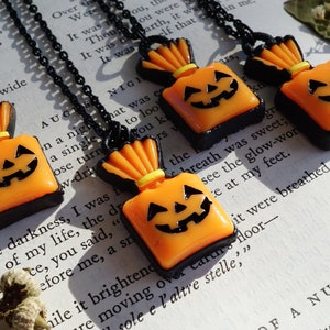 May include: Three black necklaces with orange and black pumpkin-shaped candy bag pendants. The pendants have a black face with a yellow smile and two black eyes.