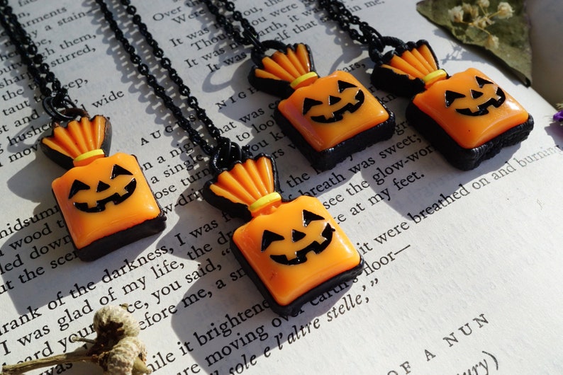 May include: Three black necklaces with orange and black pumpkin-shaped candy bag pendants. The pendants have a black face with a yellow smile and two black eyes.