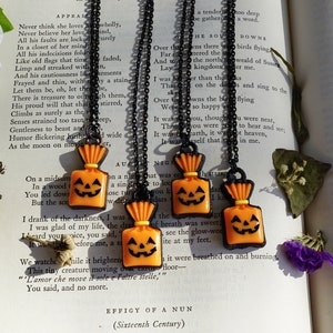 May include: Four black chain necklaces with orange and black pumpkin-shaped charms. The charms are shaped like a jack-o-lantern with a smiling face. The charms are hanging from a black chain necklace.