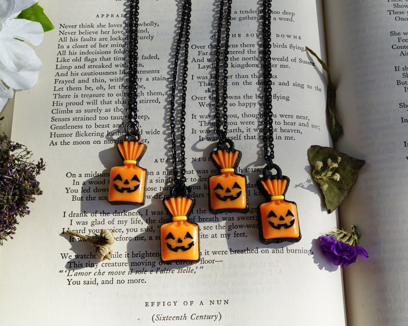 May include: Four black chain necklaces with orange and black pumpkin-shaped charms. The charms are shaped like a jack-o-lantern with a smiling face. The charms are hanging from a black chain necklace.