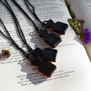 May include: Five black pendant necklaces with different shaped charms, hanging on a book with text. The charms are made of a dark, textured material and have a rustic, vintage look.