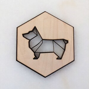 May include: A wooden hexagon-shaped coaster with a laser-cut origami-style corgi dog design. The dog is depicted in shades of gray, set against a light wood background. The coaster has a dark brown border.