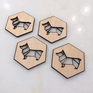 May include: Four wooden coasters with a geometric corgi design. Each coaster is hexagonal with a light wood finish and a dark outline of the corgi. The corgi design is cut out of the wood.