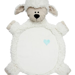 May include: A plush, white lamb-shaped baby blanket with a soft, textured exterior. The lamb features a beige face, ears, and feet, with a black nose and two small black dots for eyes. A light blue heart is embroidered on the blanket's body.
