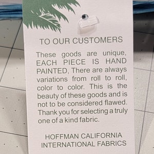 May include: A white tag with green text and a palm tree logo. The tag reads "TO OUR CUSTOMERS" and describes the unique, hand-painted fabric. The tag is from HOFFMAN CALIFORNIA INTERNATIONAL FABRICS.