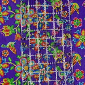 May include: Purple fabric with a repeating pattern of colorful beaded flowers and hummingbirds. A ruler is placed on the fabric to show the scale of the pattern.