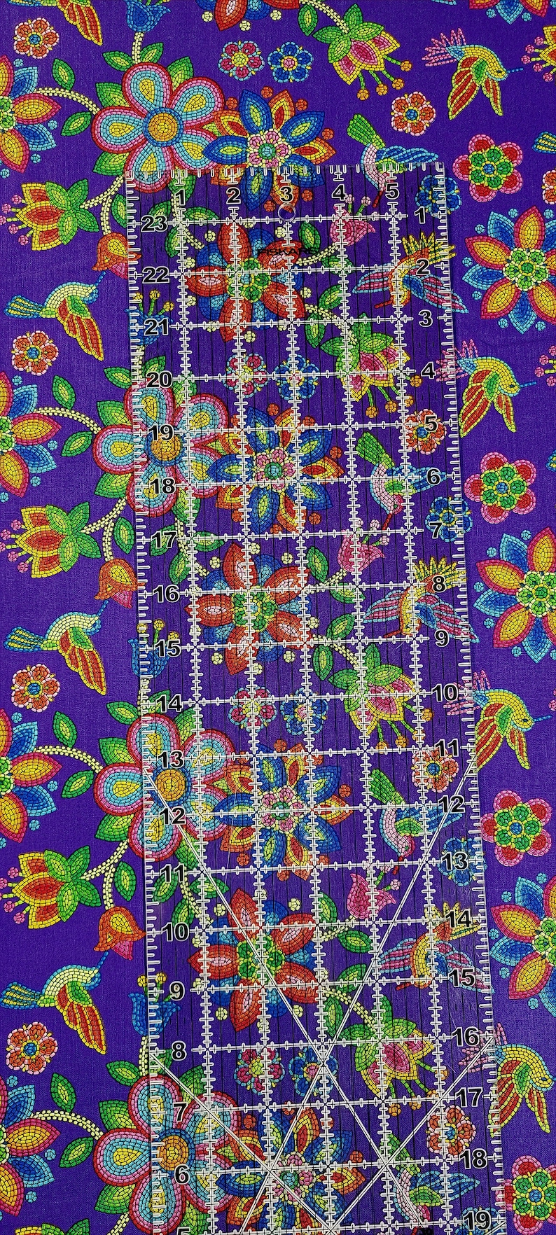 May include: Purple fabric with a repeating pattern of colorful beaded flowers and hummingbirds. A ruler is placed on the fabric to show the scale of the pattern.