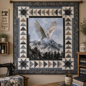 May include: A square wall quilt featuring a central printed panel of a white owl in flight over a mountain landscape. The border consists of pieced star blocks in the corners and rows of blue, gray, and white triangles surrounding the center.